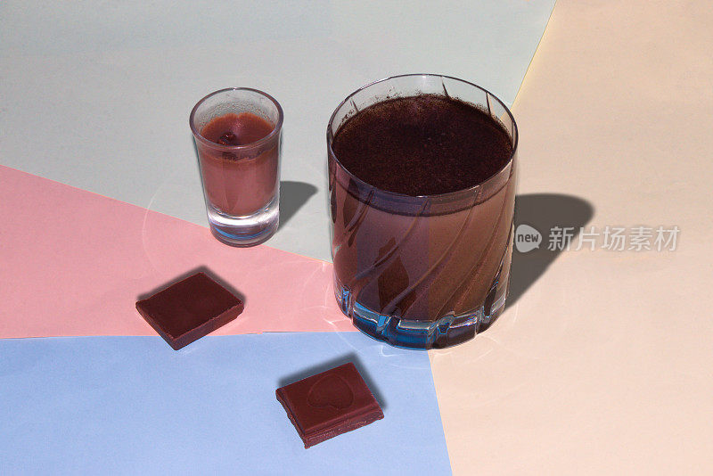 一小杯大杯的巧克力和两块巧克力，在彩色粉彩的背景上