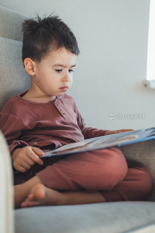 学龄男孩一边读书，一边舒舒服服地坐在沙发上做作业去学校。远程教育。关闭了。