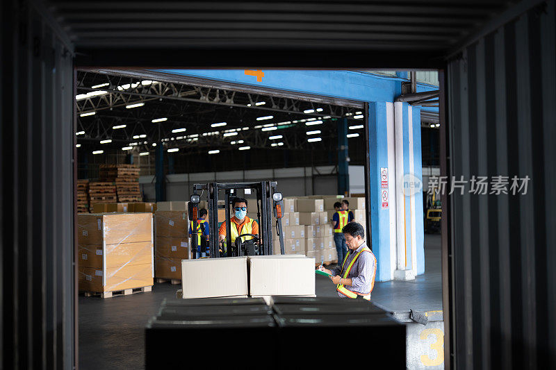 仓库工作人员打开40英尺的集装箱门，让叉车从40英尺的集装箱中取出纸箱，集装箱主管站在旁边用回形针检查清单