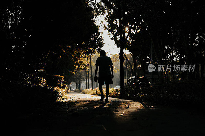 剪影后视图中成年男子步行在公园步道与背光的阳光后，例行的跑步锻炼
