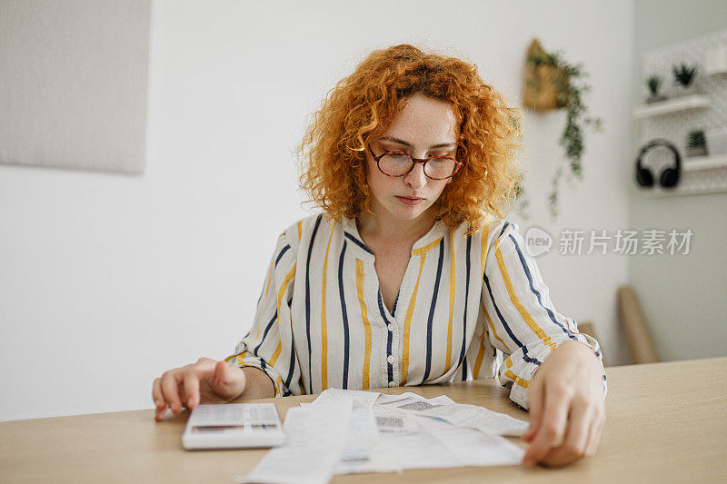 一个年轻的女人在家庭办公室计算家庭财务时看起来压力很大