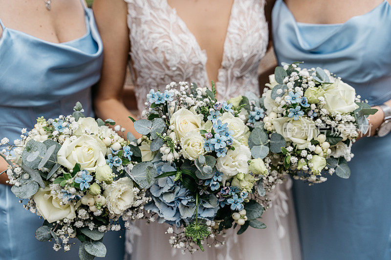 新娘和两个身穿蓝色礼服的伴娘捧着花束