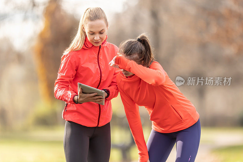 一名年轻的女教练和一名初中生正在用平板电脑检查自己的运动成绩。