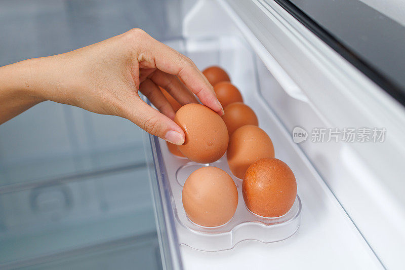 一个女人从冰箱的架子上拿出一个新鲜的鸡蛋