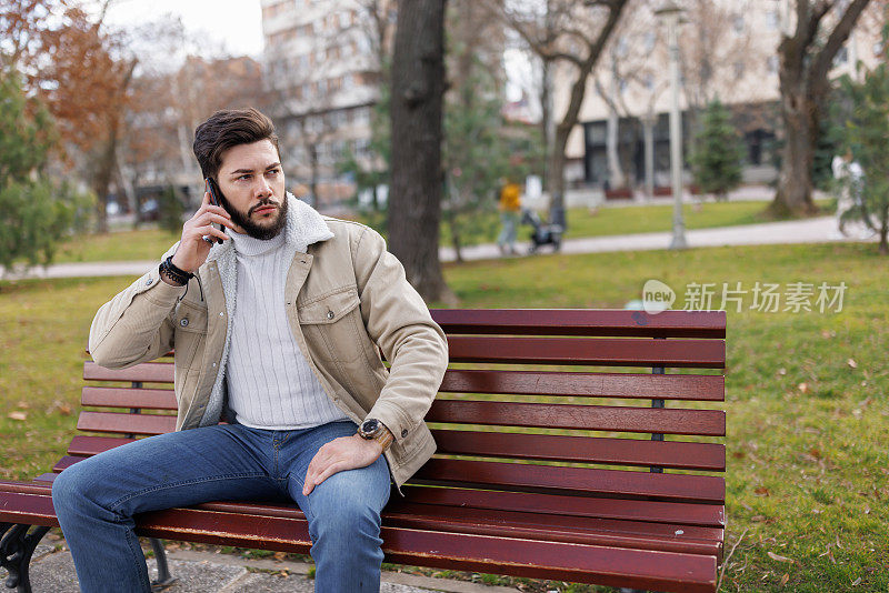 年轻人坐在城市公园的长椅上打电话