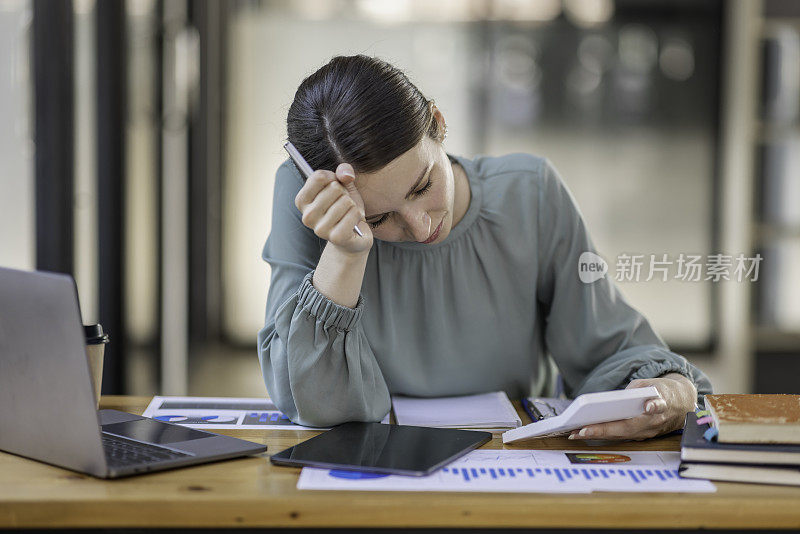疲惫的年轻商业亚洲妇女的肖像与文件税务笔记本电脑在办公室工作。悲伤，不快乐，担心，抑郁，或员工生活压力的概念
