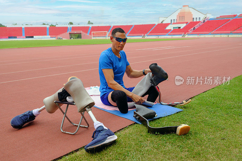 一个亚洲模范运动员的肖像，坐在体育场的跑道上，忙着安装他的跑步刀片，准备进行高强度的训练