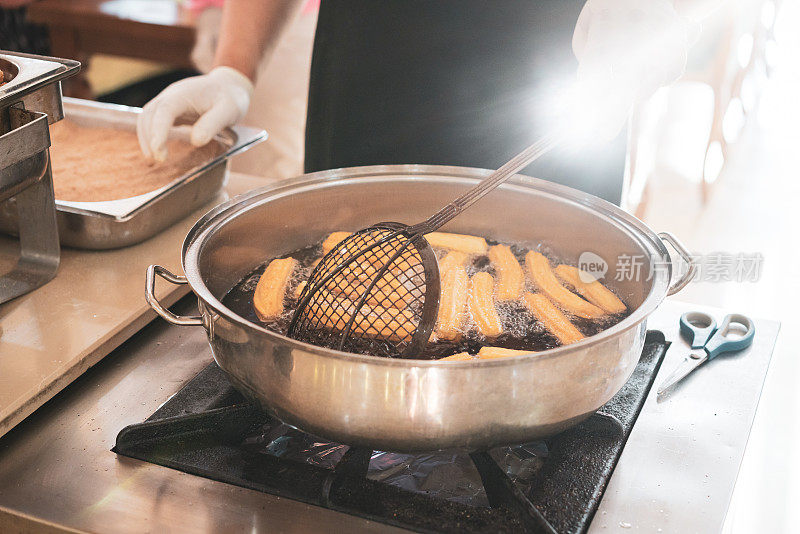 厨师将油条从沸腾的油中取出，放入金属篮子中搅拌。