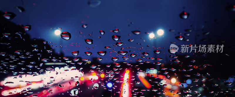 在雨中开车。雨季雨水落在汽车挡风玻璃或车窗上，背景是模糊的交通道路。雨滴落在汽车后视镜上。雨中的路。毛毛雨会降低行车能见度。