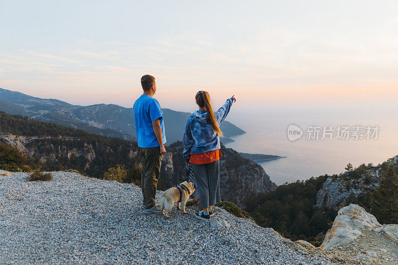 夫妇与狗的后视图在日落期间从上面考虑土耳其海的风景