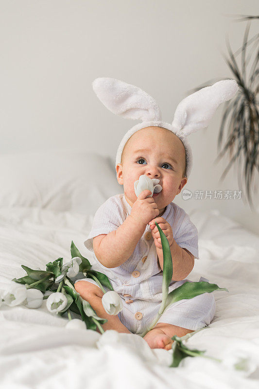 可爱的宝宝头上戴着兔子耳朵，家里的床上放着郁金香。复活节和春天时间的概念。