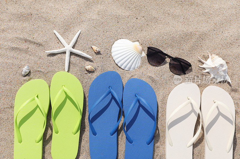 时尚的彩色人字拖，太阳镜，贝壳和海星在户外的沙滩上，平躺