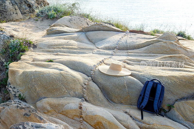 哈尔基季基上,在你的春天徒步旅行。背包和可重复使用的帽子放在海滩附近的岩石上