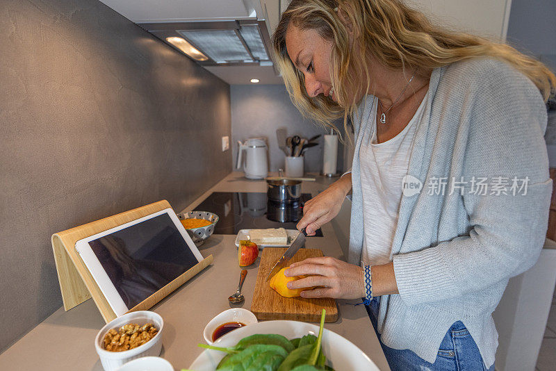 妇女在家里按照数字平板电脑上的食谱准备健康食品