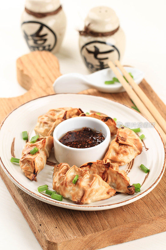 Gyoza亚洲锅贴与酱汁服务于棕色陶瓷日本风格的盘子与筷子和葱在白色木制背景。没有油的空气炸锅烹饪。