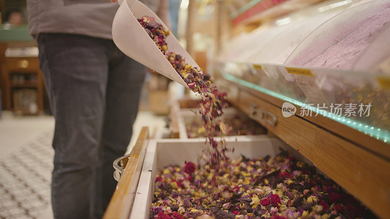 在土耳其伊斯坦布尔的大巴扎商店里，店主正往容器里倒水果和花草茶
