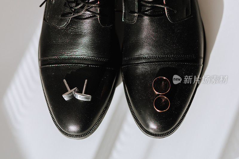 新郎在白色地板上的细节。黑皮鞋，金婚戒，袖扣