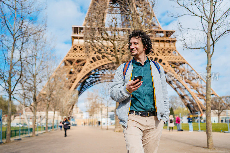 法国巴黎，一个年轻人在埃菲尔铁塔前玩手机