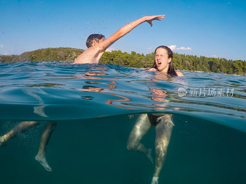 十几岁的男孩在水中浸泡他的妹妹，在海里玩耍，用可穿戴式水下相机拍摄