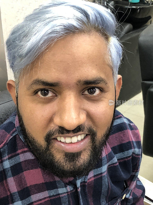 一名印度男子展示新发型的特写照片，黑色的头发被染成了金色，并被化学物质染成了蓝色和灰色