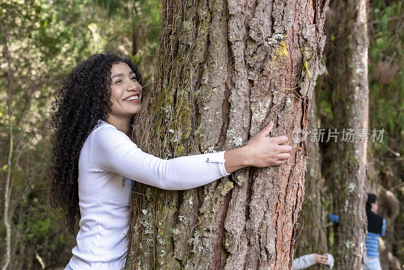 一个非洲拉丁妇女抱着树干，享受与大自然的时刻