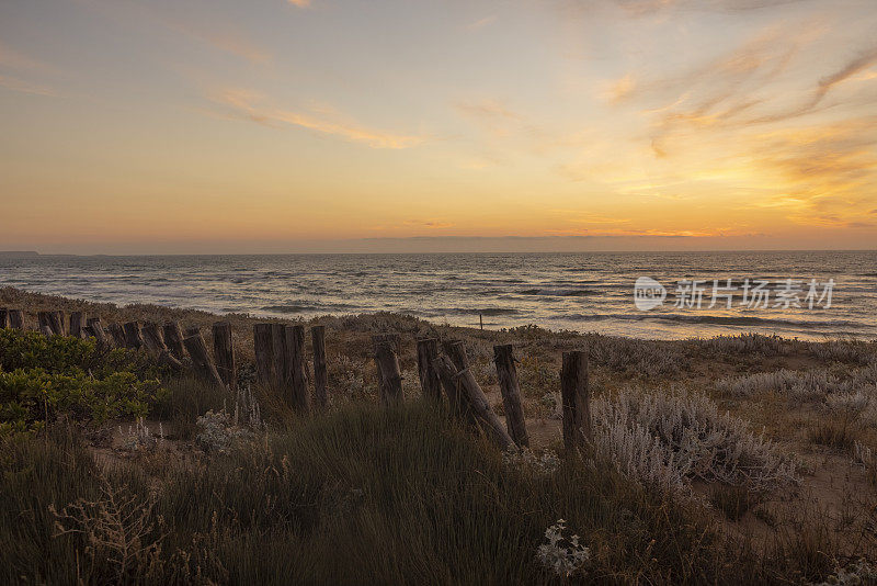 意大利撒丁岛，日落时海滩上的木栅栏。