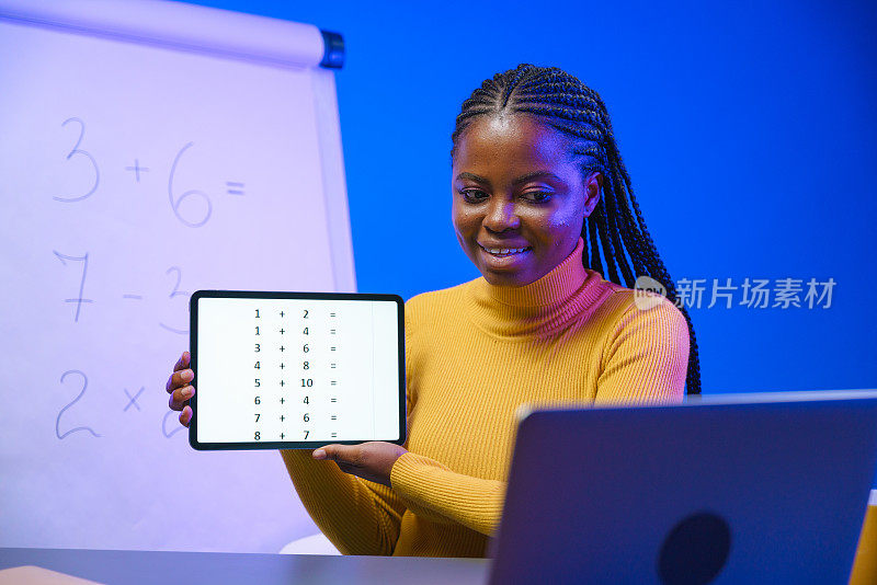一位皮肤黝黑的年轻女教师微笑着向她的笔记本电脑展示带有数学例子的平板电脑