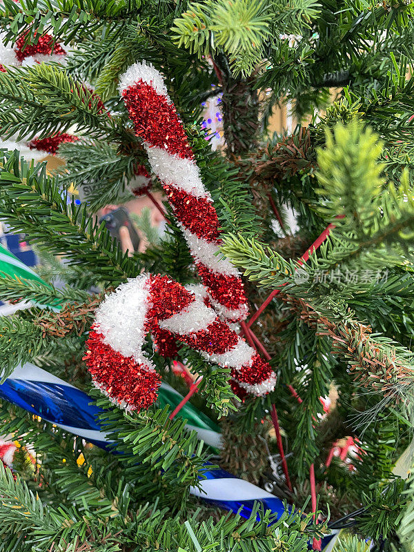 红色和白色的金属丝糖果藤挂在人造圣诞树上，绿色的塑料云杉针，模糊的白色神仙灯的背景