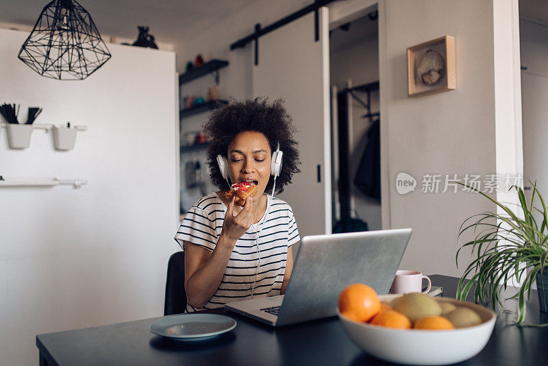 年轻的非洲女人吃着早餐，在网上工作