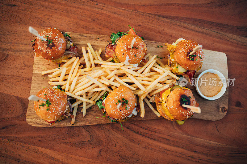 美味的带沙司的迷你汉堡，和炸薯条一起放在木板上。
