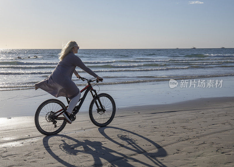 日出时，一名女子骑着自行车在空旷的海滩上骑行