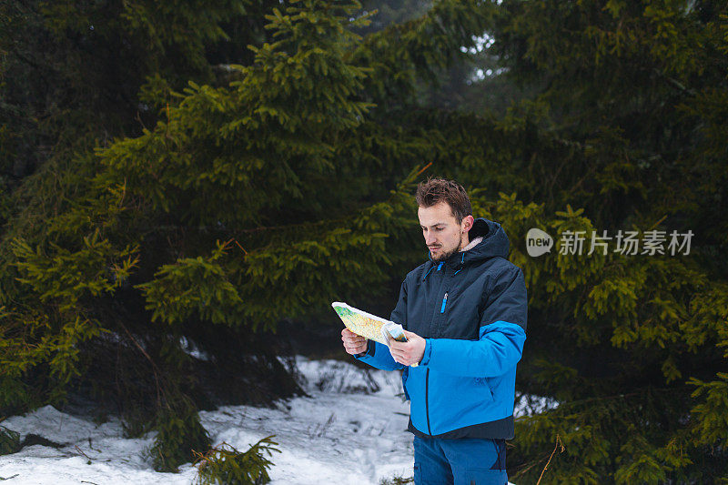 年轻的男性徒步旅行者穿着蓝色夹克，在雾蒙蒙的雪山中迷失了方向，看着地图