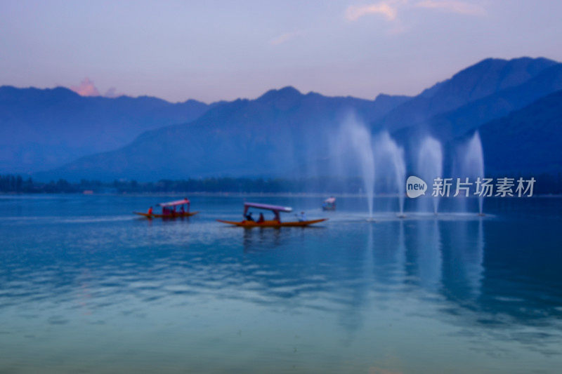 印度查谟和克什米尔达尔湖上喜马拉雅山脉的模糊倒影。下午晚些时候，游船在喷泉旁漂浮。