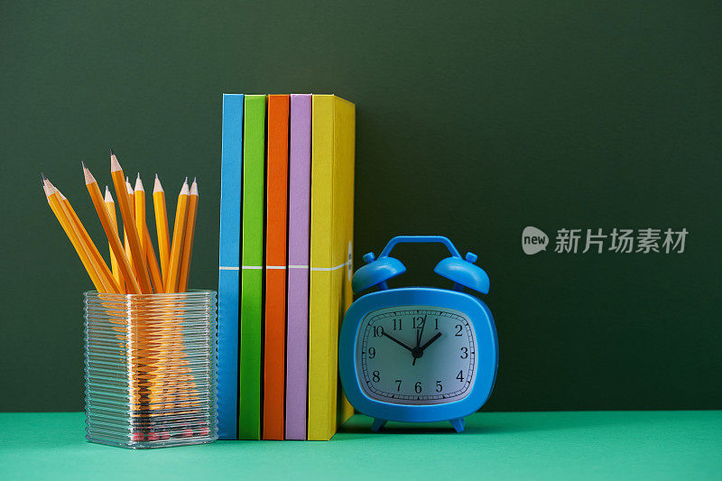 闹钟夹里有彩色的书和铅笔