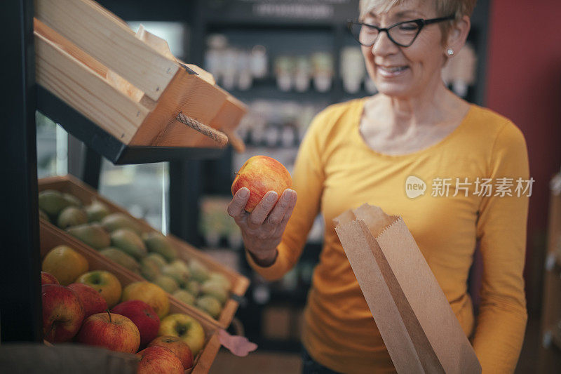 一位身着黄色上衣的高级女士在一家健康食品店购买水果。