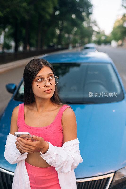 一名妇女在街上的汽车旁使用手机