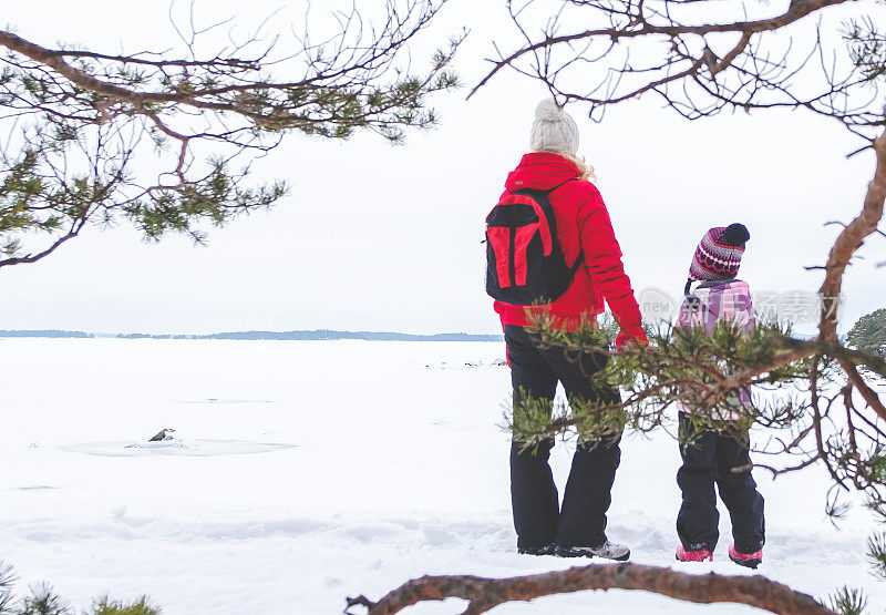 一位年轻的妇女和一个孩子走在白雪皑皑的海湾岸边。家人徒步旅行。