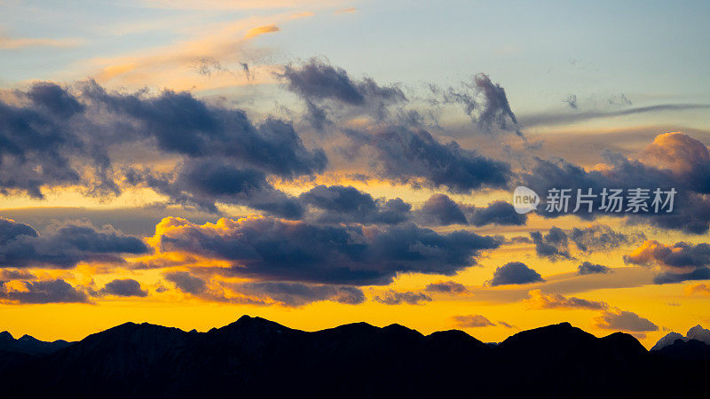 朵朵蓬松的云朵在多彩的黄昏天空中，山岭的剪影在底部
