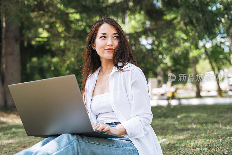 年轻的亚洲女学生自由职业者长发在城市公园的笔记本电脑上工作