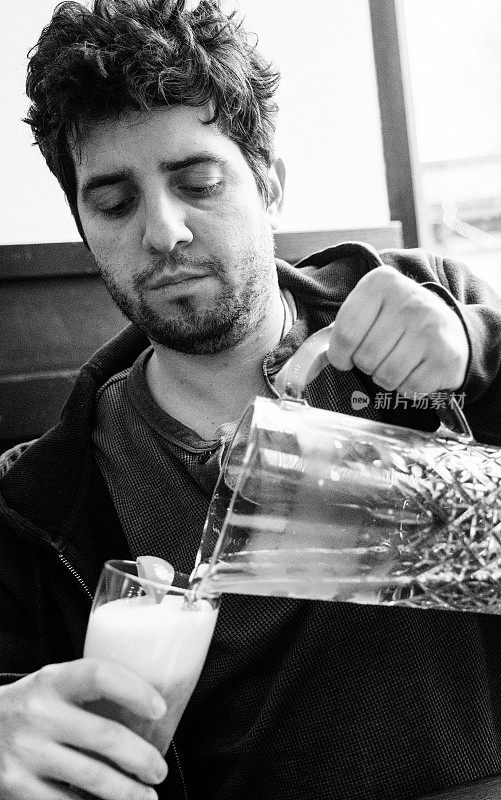 黑白照片上，一个年轻人从一个大水罐里给自己倒了一杯啤酒
