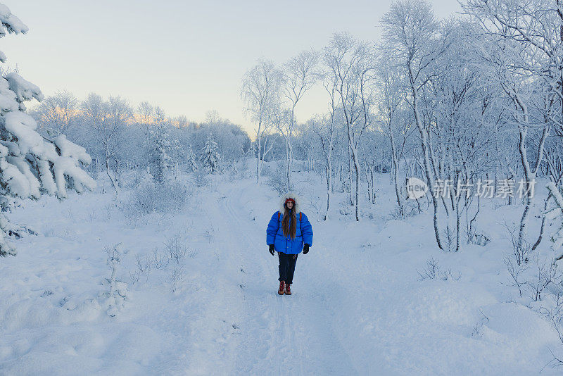 在挪威，一名女子漫步在风景优美的冬季森林中，凝视着冰天雪地