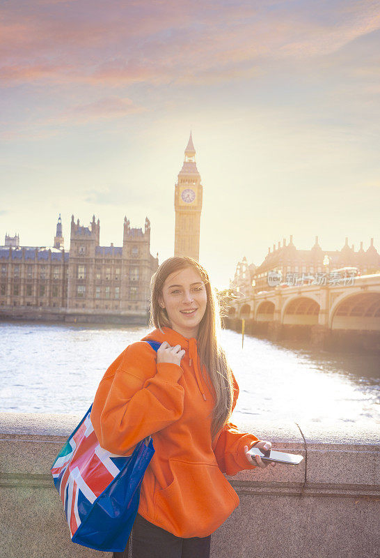 伦敦金发游客年轻女学生，英国国旗购物袋和智能手机，大本钟，议会大厦，威斯敏斯特