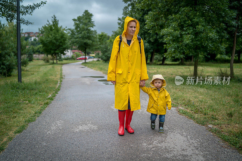 母亲和一个孩子。穿着雨衣的母子在公园里手牵着手