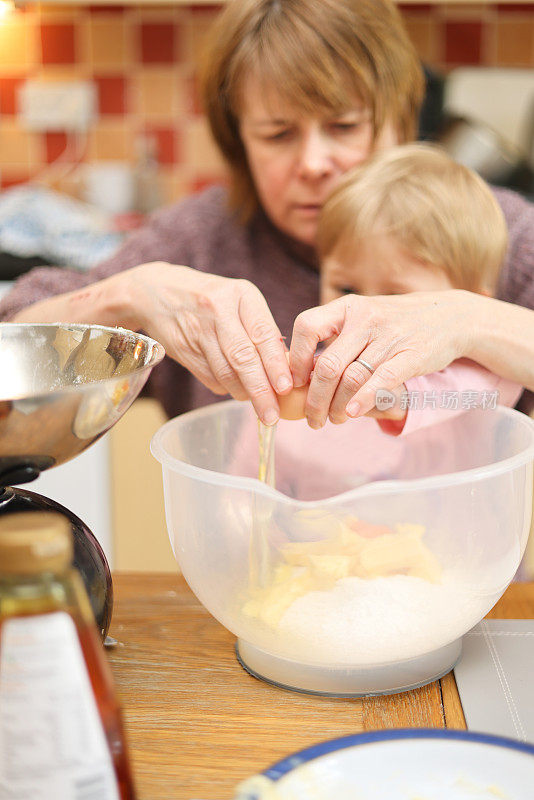 奶奶教她的孙子如何在碗里打一个鸡蛋来准备蛋糕粉