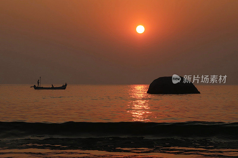 美丽的海边橙色日落的特写图像，日出反射在大海和潮湿的沙子上，水中的大型海滩岩石，渔船，潮汐反射涟漪，太阳落在海滩上