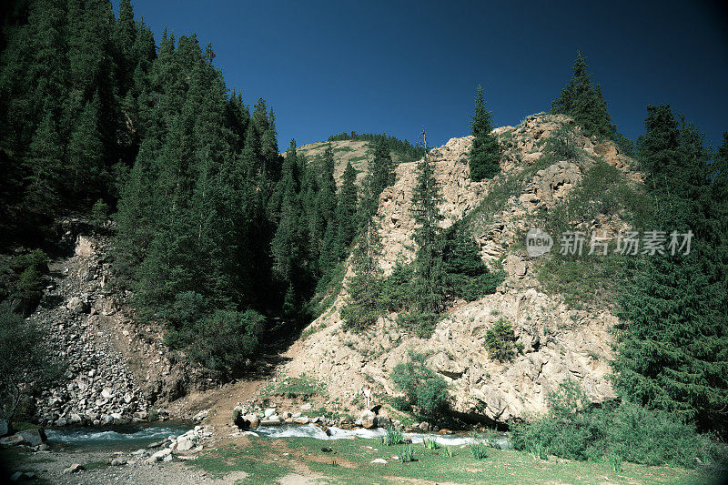 女游客在南天山狭窄峡谷的山河上方的岩石上拍摄视频