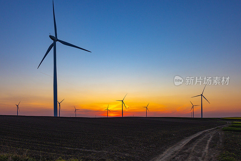 美丽的夕阳下，土路旁农田上的风力涡轮机