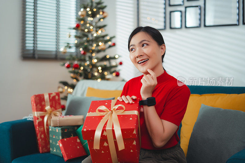 亚洲妇女在圣诞节那天高兴地收到礼物，坐在装饰着圣诞树的客厅里。