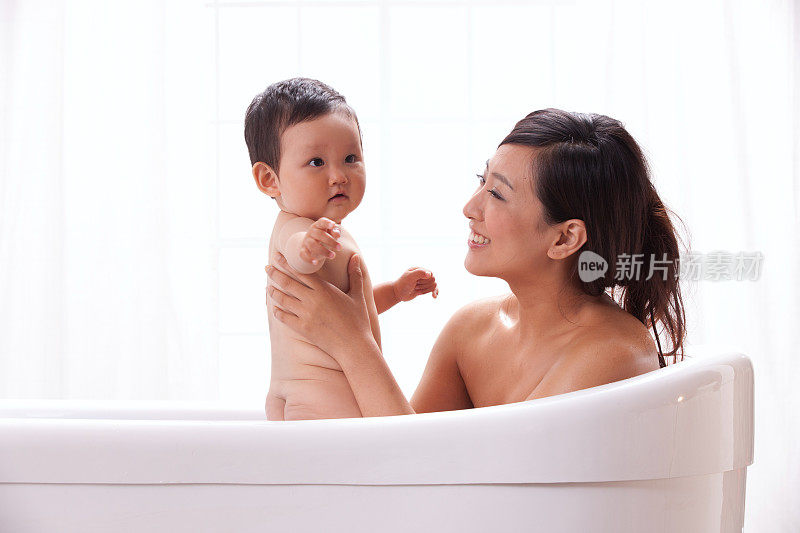 母亲和婴儿坐在浴缸中洗澡