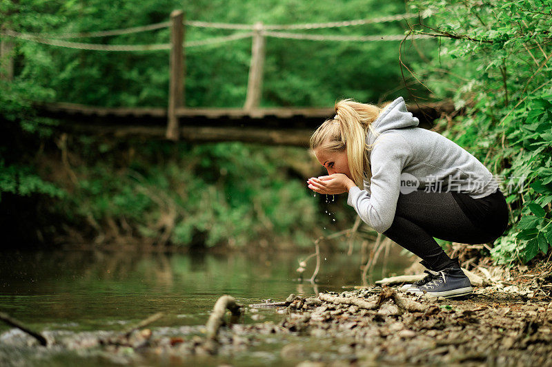 一个女人在喝着小溪里的淡水